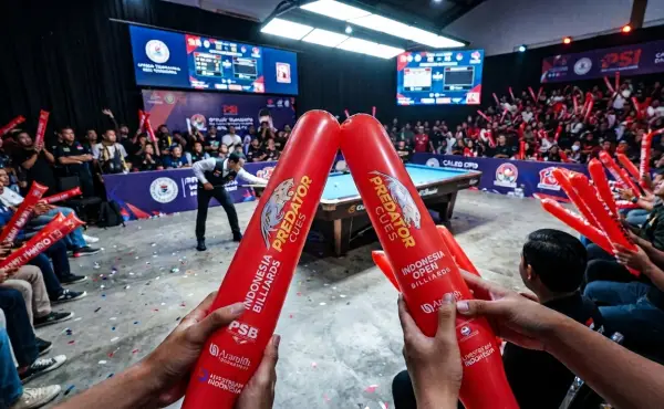 Peserta menyaksikan perlombaan biliard sambil memegang balon tepuk berwarna merah sebagai perlengkapan pendukung suasana pertandingan.