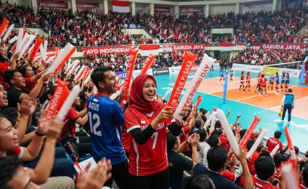Suporter menggunakan balon tepuk untuk mendukung tim pada pertandingan bola voli indoor.