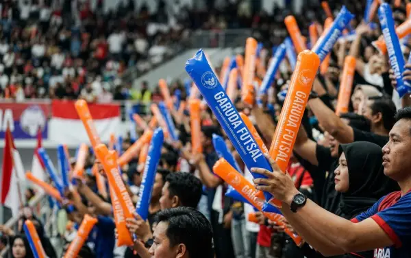 Balon tepuk warna biru dan oranye digunakan penonton untuk menyemarakkan pertandingan futsal.