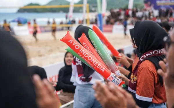 Balon tepuk warna merah dan hijau digunakan penonton untuk memberikan dukungan saat pertandingan voli pantai.