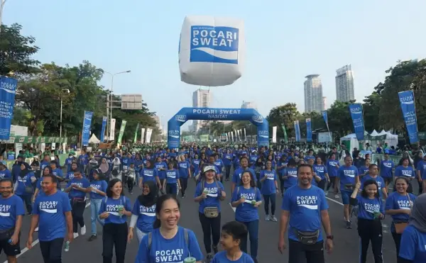 Balon udara promosi terlihat di atas kerumunan peserta jalan sehat yang mengenakan kaus seragam di area perkotaan.