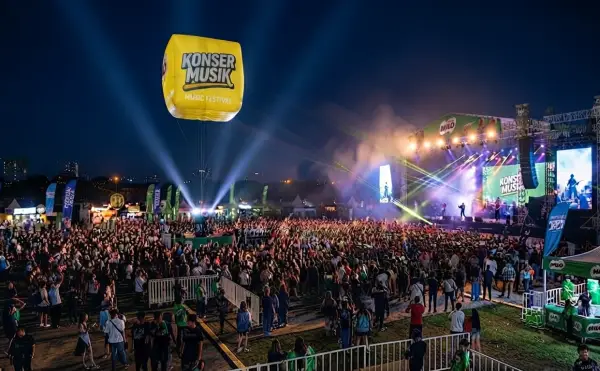 Balon tampil di atas kerumunan penonton konser musik dengan panggung dan pencahayaan yang meriah.