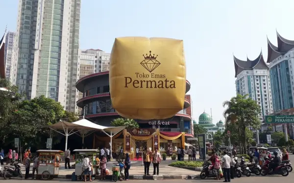 Balon udara berbentuk kubus berwarna emas digunakan sebagai media promosi toko emas di area perkotaan.
